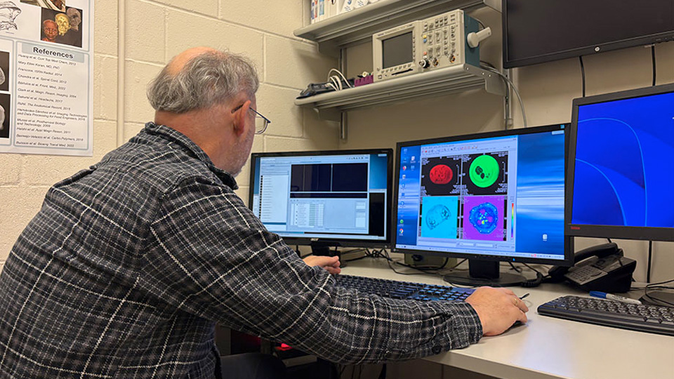 A researcher analyzing colorful MRI scan images on multiple computer monitors.