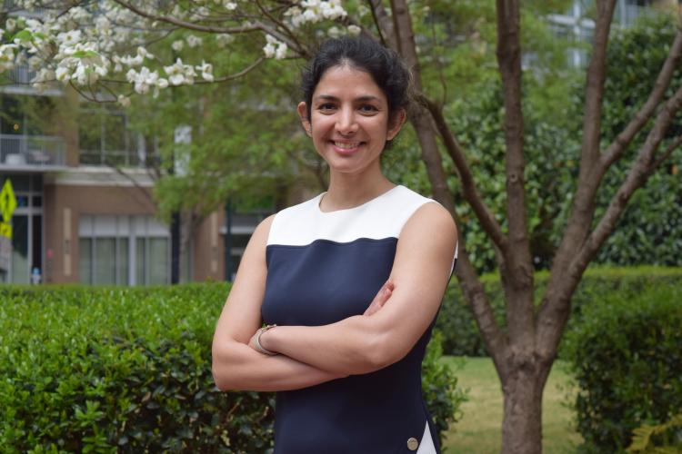 Farzaneh Najafi standing outside smiling with her arms crossed. Green foliage is visible in the background.